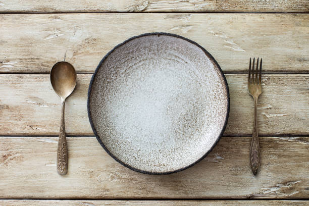 Empty ceramic plate, vintage spoon and fork on old wooden background