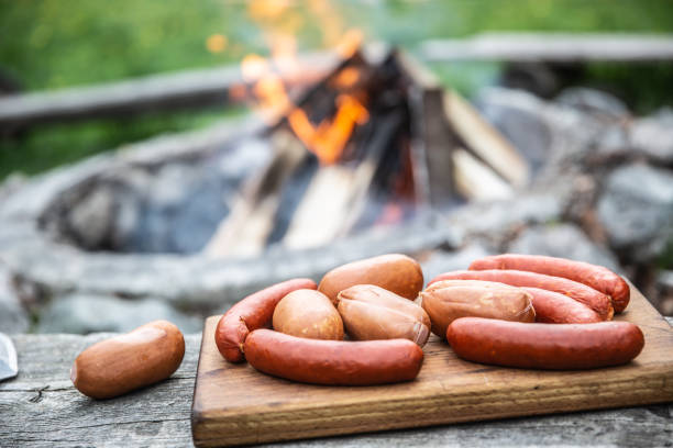 istock Sausages on a wooden cutting board ready for roasting over a campfire in the background 1279811077