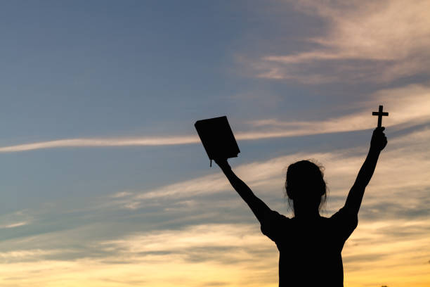 mujeres de pie sosteniendo la santa biblia por adorar a dios en el fondo del atardecer, oren al dios, concepto de silueta cristiana. - god freedom arms raised high angle view fotografías e imágenes de stock