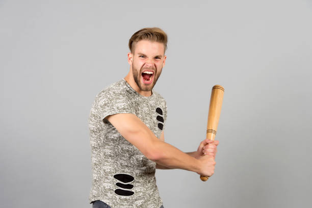 istock Bully man shouting aggressive face, grey background. Man with wooden bat ready to attack. Aggressive behaviour concept. Man bearded looks aggressive and threatening. Dangerous behaviour of hooligan 1279814198