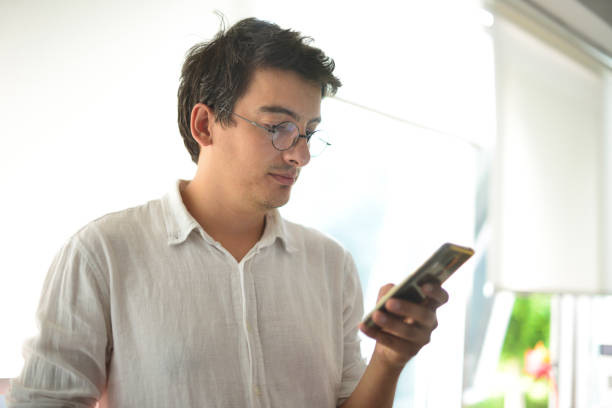 istock Young man with round glasses writing a message with a smart phone. 1279814210
