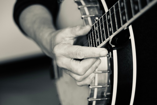 Close up of hands playing the banjo. The banjo is a stringed instrument with a thin membrane stretched over a frame or cavity to form a resonator. The membrane is typically circular, and usually made of plastic, or occasionally animal skin.