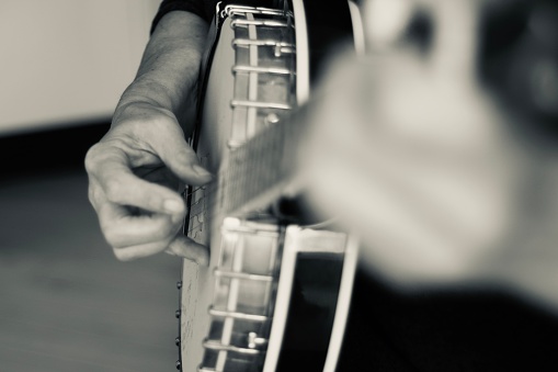Close up of hands playing the banjo. The banjo is a stringed instrument with a thin membrane stretched over a frame or cavity to form a resonator. The membrane is typically circular, and usually made of plastic, or occasionally animal skin.