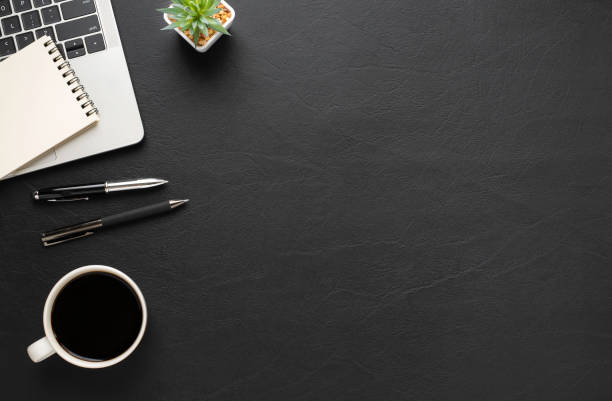 istock Top view above of Black leather office desk table with keyboard, notebook and coffee cup with equipment office supplies. Business and finance concept. Workplace, Flat lay with blank copy space. 1279819027