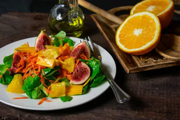 fresh and healthy fruit vegetable salad with lettuce, figs, oranges and carrots served on a plate - ready to eat