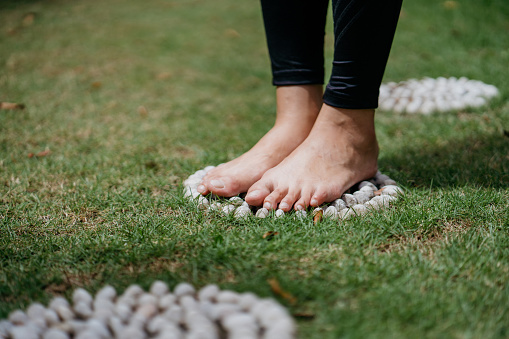 Close up of young asian woman exercising while standing on pebble path for reflexology