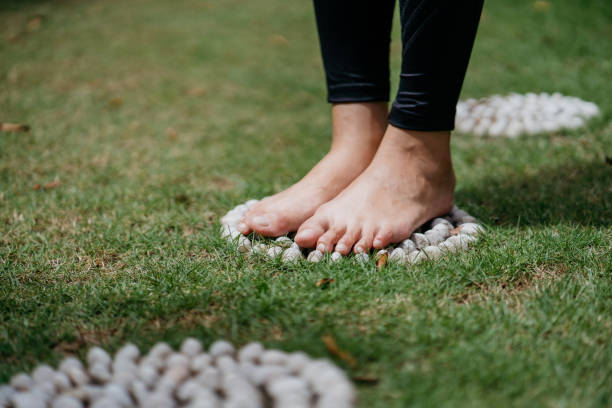 Close up of young asian woman exercising while standing on pebble path for reflexology Close up of young asian woman exercising while standing on pebble path for reflexology reflexology stone massaging human foot stock pictures, royalty-free photos & images