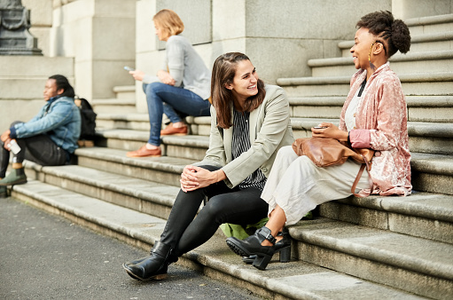 Shot of female friends sitting on city stairs and chatting