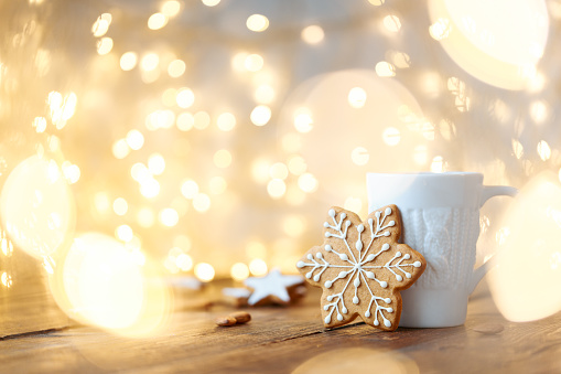 A beautiful white mug with a knitted print and a ginger cookie with icing in the shape of a snowflake on a background of garlands