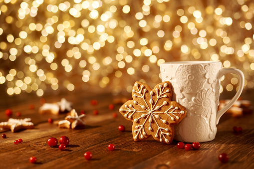 White mug with cocoa and cookies in the shape of snowflakes, and cranberries scattered around