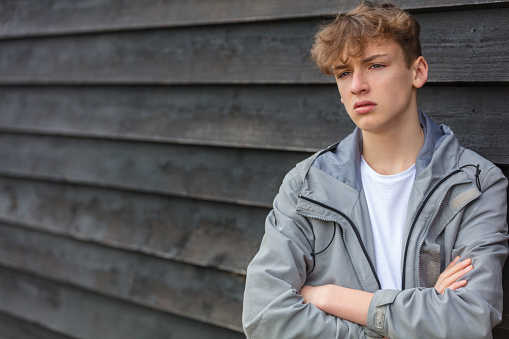 Serious male boy teenager outside leaning against a wall wearing a hoodie looking sad, moody, thoughtful or depressed