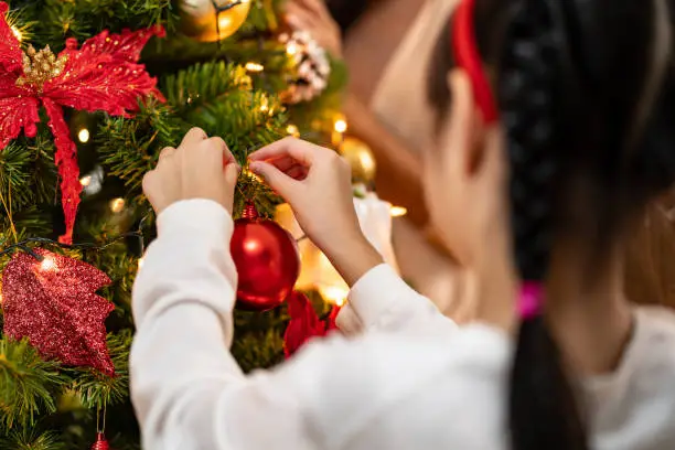 Close up hand little asian girl decorating a Christmas tree with ornament preparing for season greeting of Merry Christmas and Happy Holidays. Multigenerational Family engage and happiness concept.
