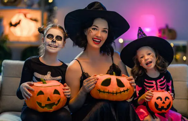 Mother and kids having fun at home. Happy family celebrating Halloween. People wearing carnival costumes and makeup.