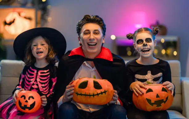 Father and kids having fun at home. Happy family celebrating Halloween. People wearing carnival costumes and makeup.