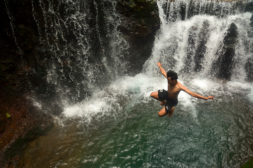 Caucasian man in swimsuit balancing near the falling water streams flowing on black volcanic stone cascades. Rochester Falls waterfall - popular tourist spot in Savanne district in Mauritius.