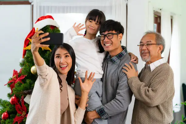 Multigenerational asian Family ,Mom Dad daughter girl and grandfather ,selfie with a Christmas tree after decorate the Christmas ornament prepare season greeting of Merry Christmas and Happy Holidays.