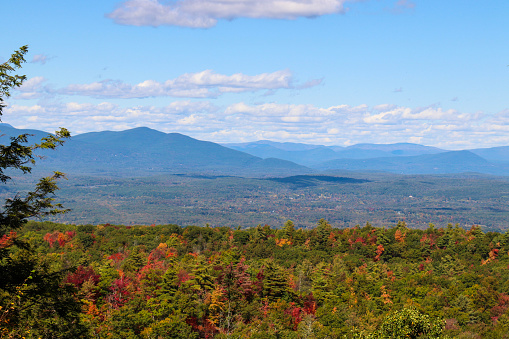 Photo with autumn colors on the trees with a beautiful lake, mountains, and sky in a New York state park - Catskill mountains in the backgroud