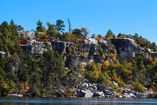 Photo with autumn colors on the trees with a beautiful lake, mountains, and sky in a New York state park - view of cliffs from across the lake