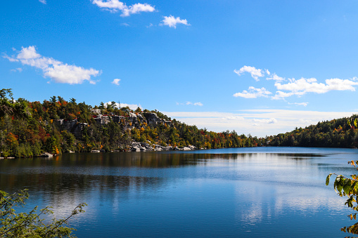 Photo with autumn colors on the trees with a beautiful lake, mountains, and sky in a New York state park - beautiful wide-angle view to highlight the entire lake