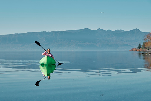 Woman relaxing in a Kayak in the middle of calm lake. Copy space and blue natural background