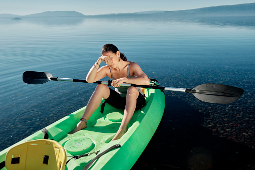 Woman sitting in a kayak on the shore of a lake tired and exhausted. Concept of sports and recreation