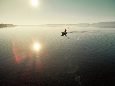 Aerial view of the silhouette of a woman floating in a green kayak in the middle of a large lake in the rays of a beautiful sunset