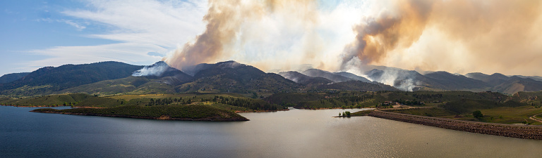 Panoramic view of a wildfire burning through the dry forests and threatening houses and buildings in the mountains