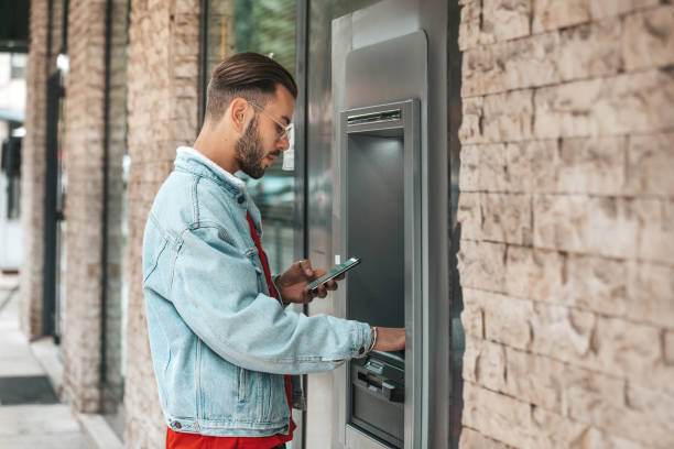 Young man withdrawal money from a bank ATM Young man withdrawal money from a bank ATM in the city streets. banks and atms stock pictures, royalty-free photos & images