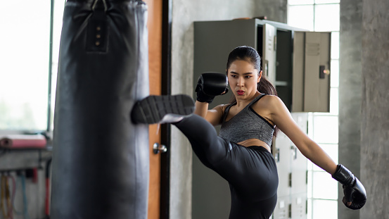 Strong muscle Asian boxing woman kick boxing to huge punching bag at fitness gym.  Athlete girl practice Muay Thai for bodybuilding and healthy lifestyle concept. workout in sport club.