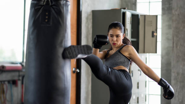 Athlete woman kick boxing training in gym Strong muscle Asian boxing woman kick boxing to huge punching bag at fitness gym.  Athlete girl practice Muay Thai for bodybuilding and healthy lifestyle concept. workout in sport club. kickboxing stock pictures, royalty-free photos & images