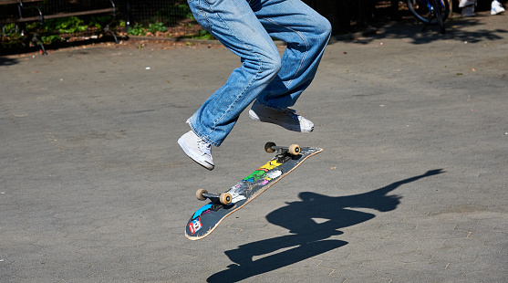 New York, NY - September 8 2020: A young skateboarder practices his tricks in Washington Square Park, New York. This shot is a detail of the trick, showing the young man's legs, his skateboard and his shadow on the pavement.