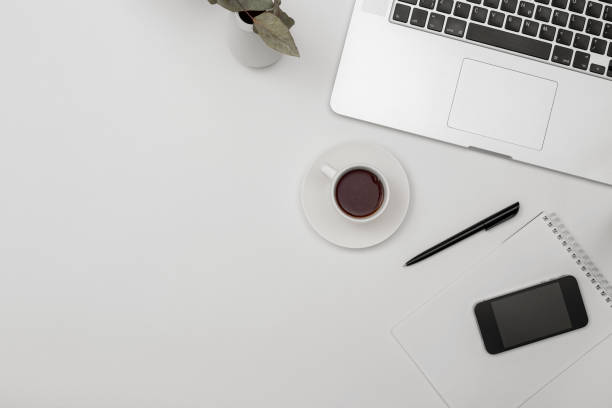 istock Desk office with laptop, blank notepad, coffee cup and pen on white table. Flat lay top view copy space. 1279837198