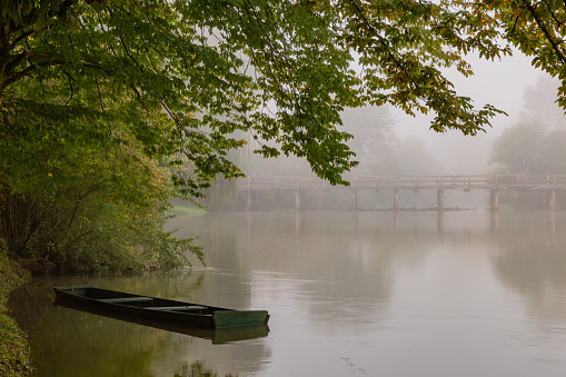 Side view of a wooden bridge creating a perfect reflection on the water surface, shrouded in dense fog