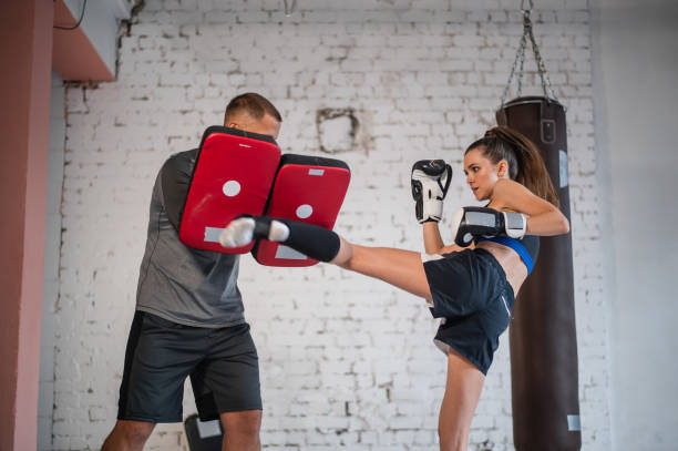 training of a professional female fighter. the girl works out a kick on the paw, which is held by her individual trainer - boxing combative sport defending protection imagens e fotografias de stock