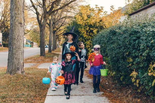 travessuras ou gostosuras. mãe com filhos vai fazer doces ou travessuras no feriado de halloween. mãe com crianças fantasiadas de festa com cestas indo para casas do bairro para doces, guloseimas. - figurino - fotografias e filmes do acervo