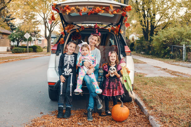 トリックやトランク。車のトランクでハロウィーンを祝う家族。伝統的な10月の休日を屋外で祝う3人の子供を持つ母親。社会的距離と安全な代替のお祝い。 - 6 11 months ストックフォトと画像