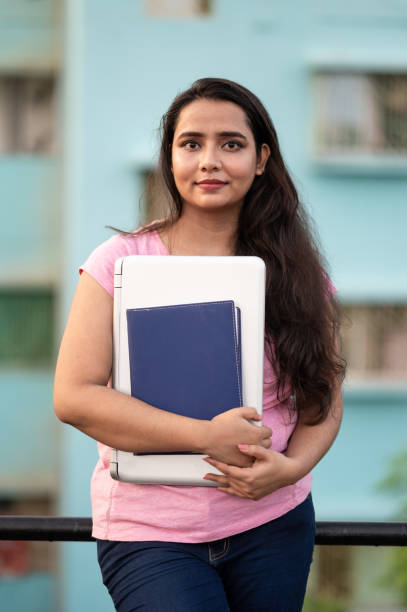 istock Smiling young female college student with book and laptop 1279850744
