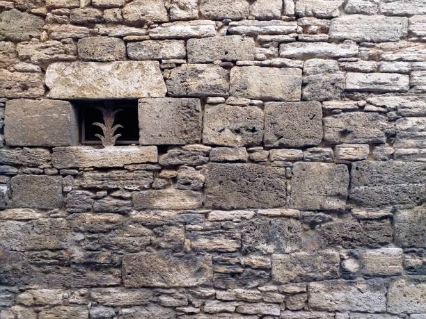 Small window in the medieval stone wall. Old historic natural stone facade for background or texture. Detail of rustic architecture and simple construction.