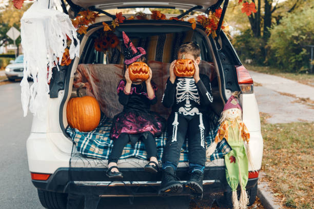 トリックやトランク。車のトランクでハロウィーンを祝う家族。伝統的な10月の休日を屋外で祝う3人の子供を持つ母親。社会的距離と安全な代替のお祝い。 - 6 11 months ストックフォトと画像