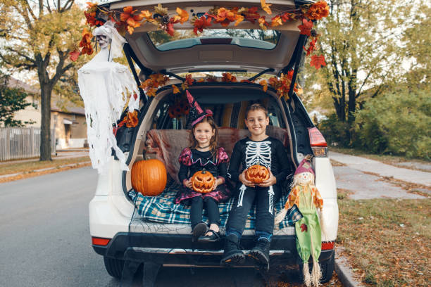 トリックやトランク。車のトランクでハロウィーンを祝う家族。伝統的な10月の休日を屋外で祝う3人の子供を持つ母親。社会的距離と安全な代替のお祝い。 - 6 11 months ストックフォトと画像