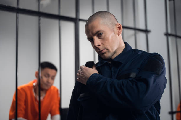 A prison guard in full ammunition communicates with his partner on the radio. In the background, a prisoner in a cell A prison guard in full ammunition communicates with his partner on the radio. In the background, a prisoner in a cell. prison guard stock pictures, royalty-free photos & images