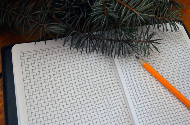 Open notebook for notes, pencil. A branch of a Christmas tree in the background. Winter postcard