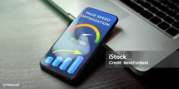 Mobile Page Speed Optimization Concept Website Loading Time Image For Internet Seo Mobile Phone Lying On A Black Wooden Table Next To The Laptop And On The Screen Accelerometer With High Values Stock Photo - Download Image Now
