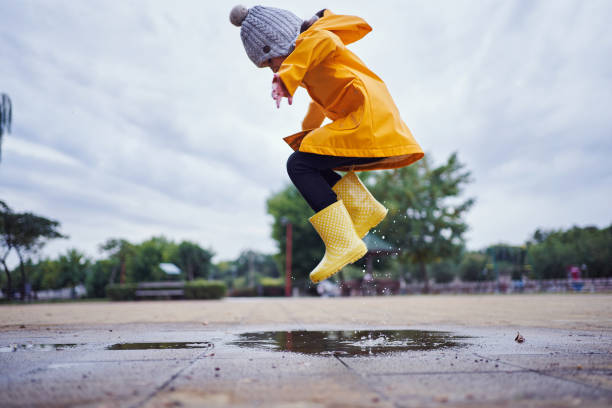 Mid-air shot of a child jumping in a puddle of water wearing yellow rubber boots and a raincoat in autumn stock photo