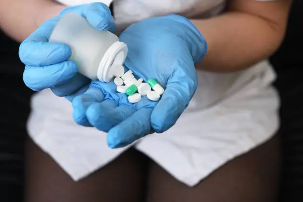 Male medicine doctor hands in blue gloves holding and offering pile of pills fall out from jar. Panacea and patient life save, legal drug store, prescribe treatment, contraception concept