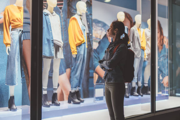 소녀는 가게 밖에 서서 마네킹에 있는 여성 옷을 바라보고 있다. - mannequin clothing window display fashion 뉴스 사진 이미지