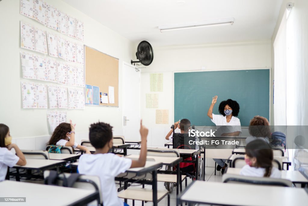 Teacher teaching in classroom respecting social distancing between students Education Stock Photo