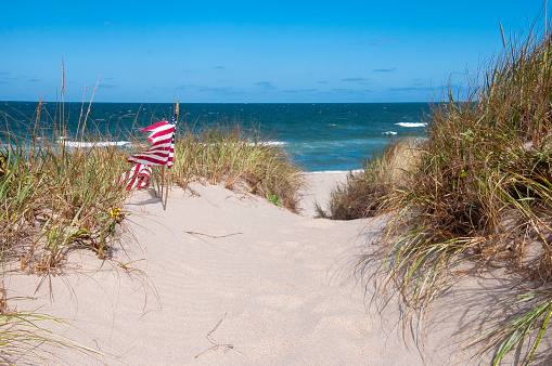 A pair of flags blown by an offshore wind flutter along a trail through the dunes leading to a empty Cape Cod beach.