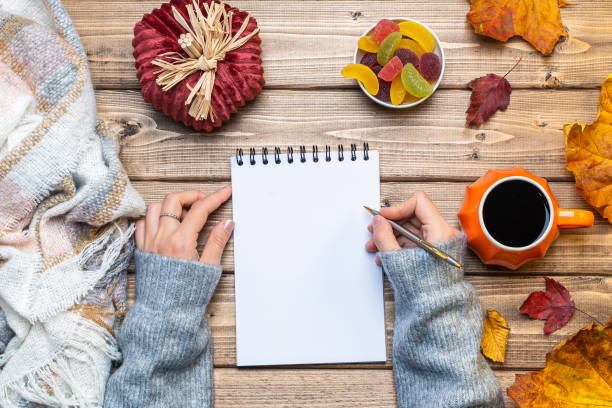 istock Desktop mock up planner. Top view composition with woman's hands in sweater, pumpkin styled cup of coffee and autumn themed decoration, fallen leaves on wooden background. Flat lay, copy space. 1279870594