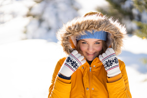 Beautiful, young woman in the mountain. She is wearing yellow parka with her hood on and interesting winter gloves.